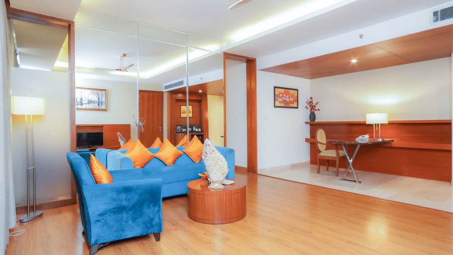 A comfortable hotel suite living area with a blue sofa and warm wooden flooring at The Conway, Meerut.