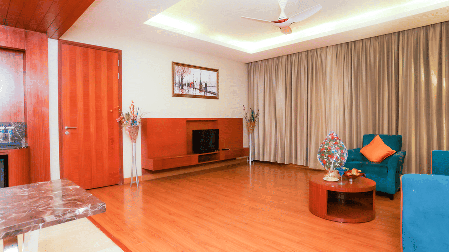 A spacious hotel suite living room with blue sofas and wooden flooring at The Conway, Meerut.
