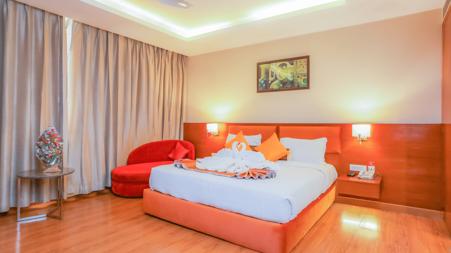A well-appointed hotel suite bedroom with a large bed and a red accent chair at The Conway, Meerut.
