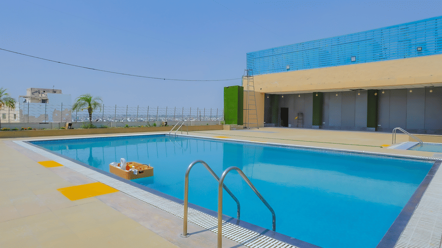 A clear blue swimming pool with an orange inflatable float, under a bright sky at The Conway, Meerut
