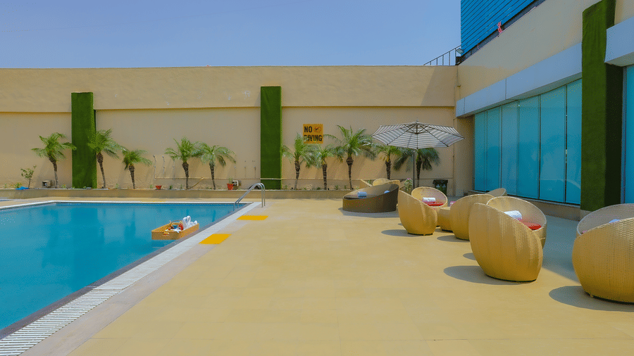 The sparkling outdoor swimming pool with yellow floating loungers and palm trees at The Conway, Meerut.