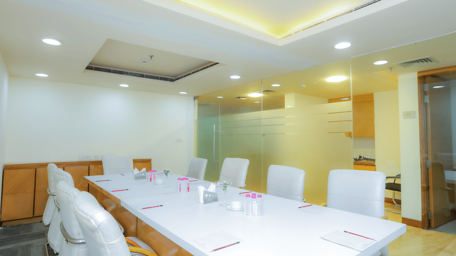 A modern meeting room featuring a large white table and comfortable chairs, brightly lit at The Conway, Meerut.