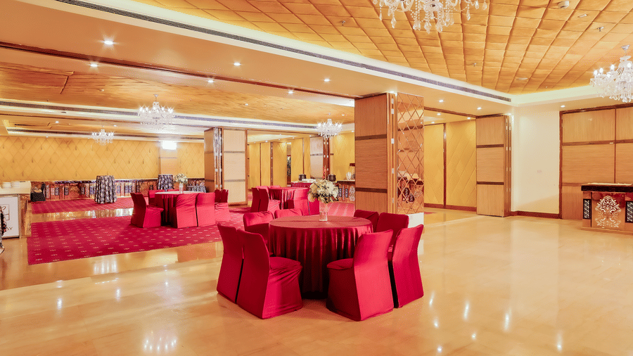 A large banquet hall set up with red tables and chairs, ready for an event at The Conway, Meerut.