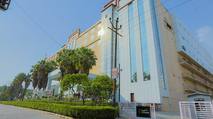 The modern exterior of The Conway hotel, visible from the street with palm trees at The Conway, Meerut.
