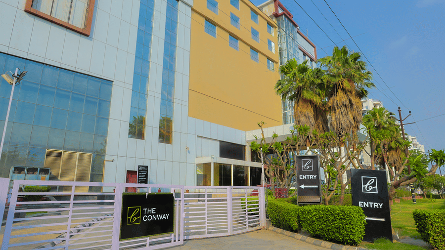 The secure entrance gate of The Conway hotel, showing the main building and palm trees at The Conway, Meerut.