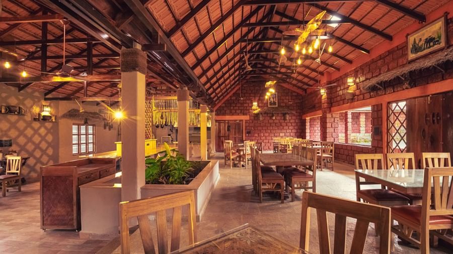 An interior shot of a dining hall with a high wooden ceiling and many tables and chairs at The Copper Edge - Eco Resort, Coorg.