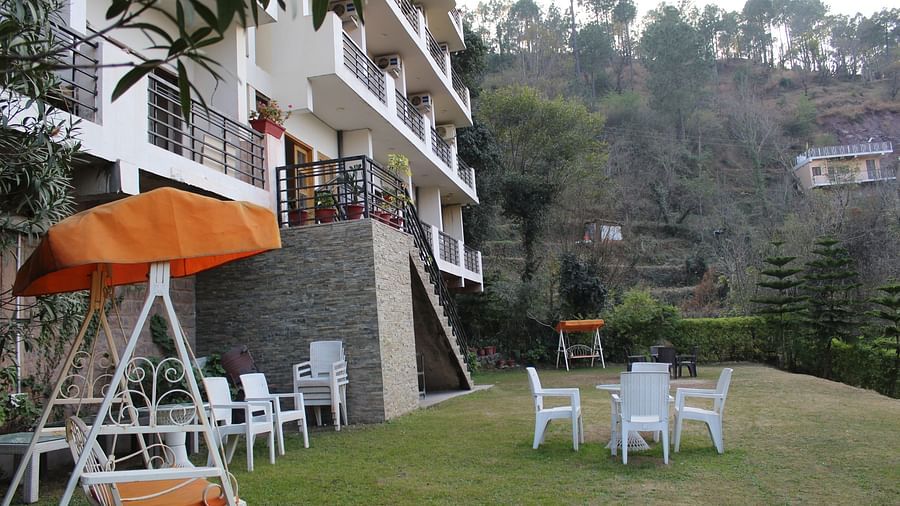 A lush green outdoor seating area with garden chairs, a swing, and a scenic backdrop at Dagshai Manor Kasauli - Inde Hotels.