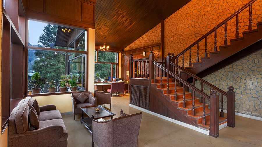 a lobby with a sofa and a table with large windows offering forest views - The Earl's Court, Nainital