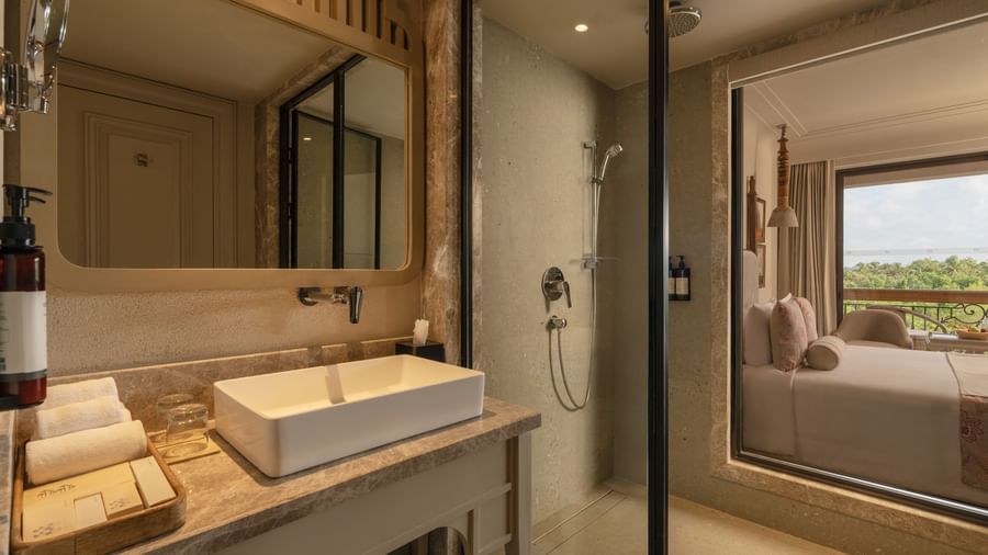 A neatly-kept vanity area with a rectangular mirror above it at the Classic Room (Diwa), seaprated by a glass partition at The Evren, Vagator.