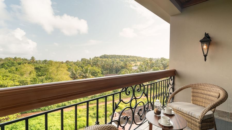 An expansive balcony with 2 arm chairs and a coffee table overlooking at the lush green lawn from the Classic Room (Diwa) at The Evren, Vagator.