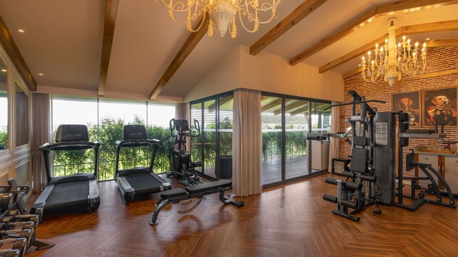 A wide-angle shot of the full-equipped gym at The Evren, Vagator, featuring elegant chandeliers hanging from the ceiling.