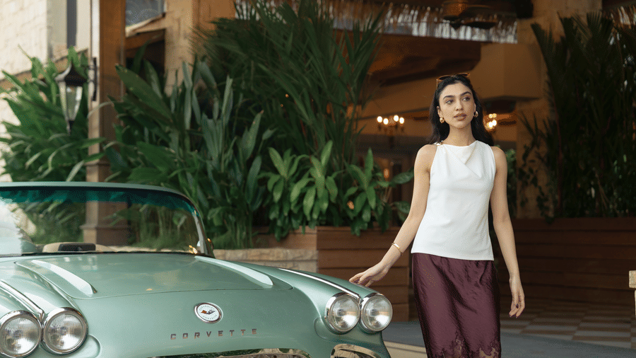 A woman standing next to a parked vintage car at an entrance area with tall plants and a covered roof at The Evren, Vagator.