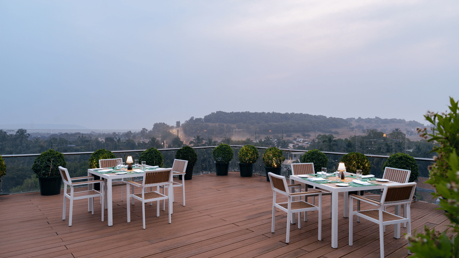 An outdoor rooftop dining at The Evren with table seating, planters along the edge, and distant landscape views.
