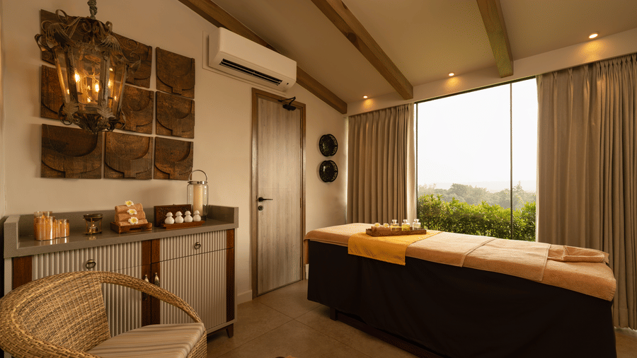 A spa room at The Evren with a massage bed, soaking tub, vanity counter, and a large window opening to greenery.