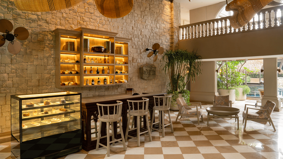 The Suenos de Cafe dining area at The Evren with a service counter, high stools, display shelves, and checkered flooring.