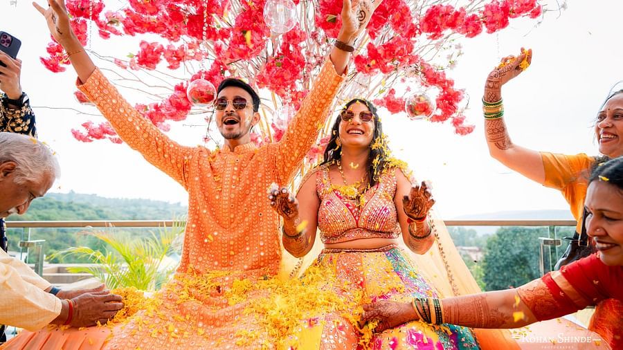 A couple in ethnic attire dances joyfully amidst a shower of flower petals, surrounded by celebrating guests with raised hands - The Grand Legacy Resort and Spa