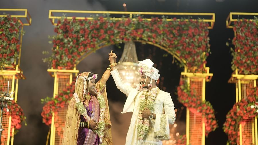 A traditionally dressed couple exchanges vows under an ornate, flower-covered mandap. Priests chant, and attendees observe the Hindu wedding ceremony - The Grand Legacy Resort and Spa
