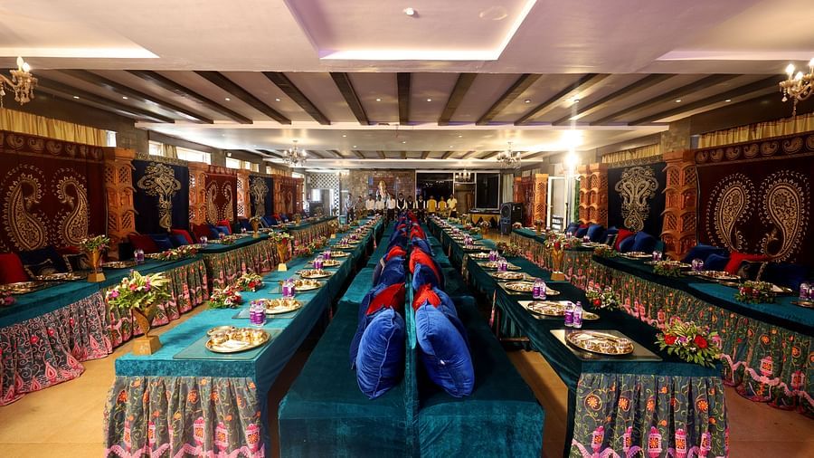 A banquet hall featuring a decorated long table where plates and water bottles are placed and a long chair with cushions paired with it at The Grand Legacy Resort & Spa