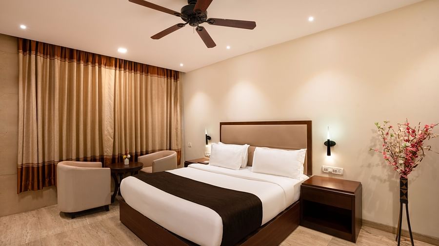 Shot of a spacious room with neutral toned walls featuring a king size bed, two small sofas, a centre table, flower vase and a side table | The Grand Legacy Resort and Spa
