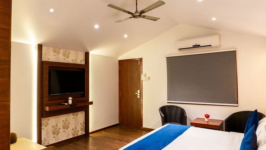 Lawn View Tent Room at The Grand Legacy Resort and Spa featuring wooden flooring, a wall-mounted TV, blue-accented bed, seating area, ceiling fan, and window blinds.
