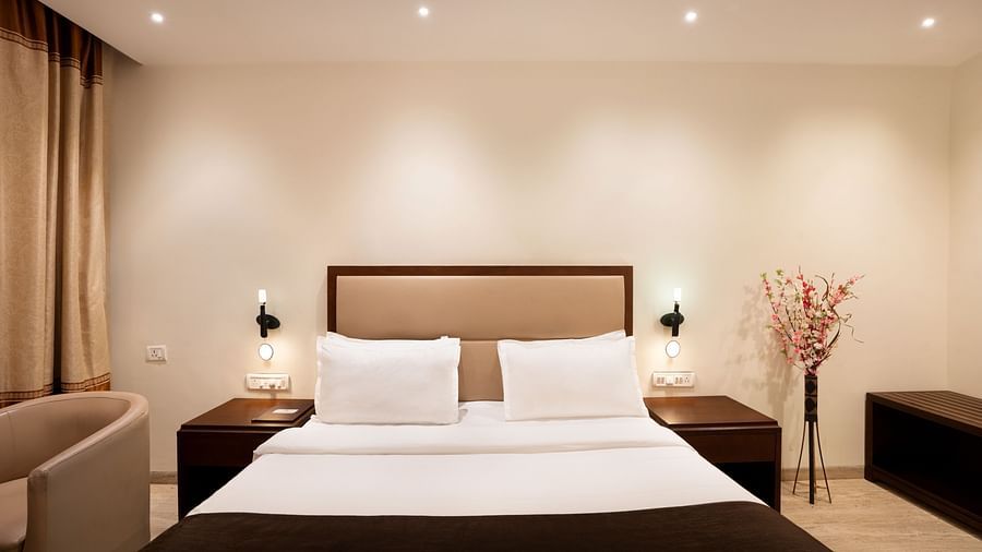 Shot of a king size bed in a well lit room with a flower vase in the corner | The Grand Legacy Resort and Spa