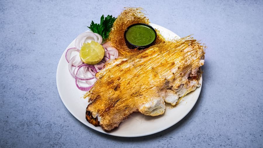 A plate of appetiser sided with onion rings, lemon wedge, and green chutney placed on a grey surface at The Hamuse Hotel, Kodaikanal.