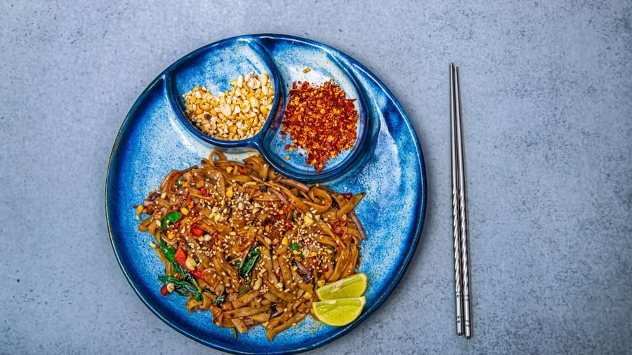 A blue plate with noodles garnished with herbs and served with crushed peanuts and chili flakes in small side compartments at The Hamuse Hotel, Kodaikanal.
