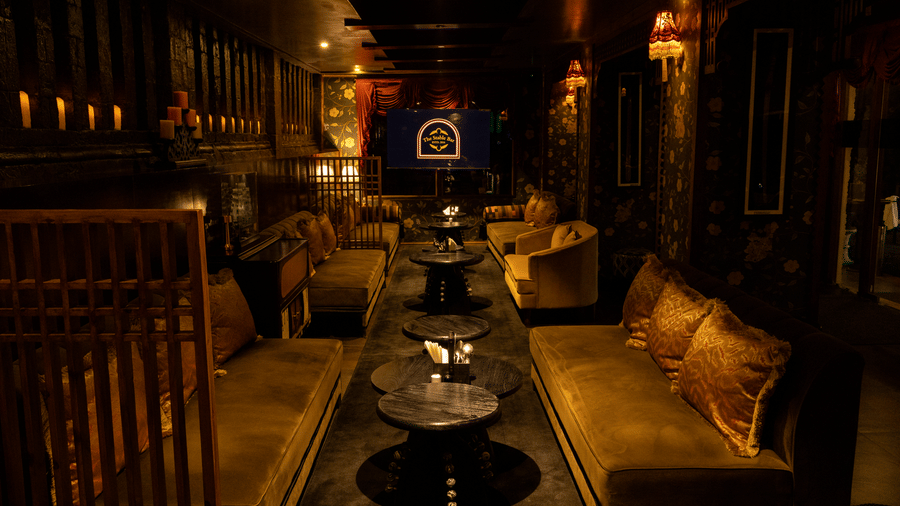 A dining space with sofas, tables, lamps and a television displaying stable bar. | The Heritage Club, Tripura, Castle, Shillong