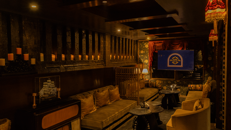 A dining space with cushions, tables, and a wall-mounted television showcasing, The Stable Bar.