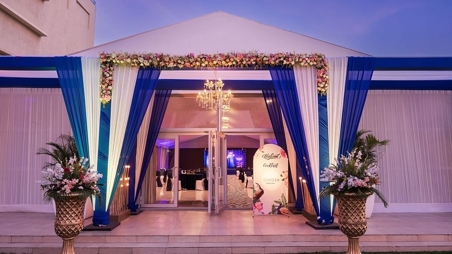 an entrance to a hall with a sign board beside the entry gate and blue and white curtains in front of the entrance - The Hideaway Banquets & Lawns, Greater Noida
