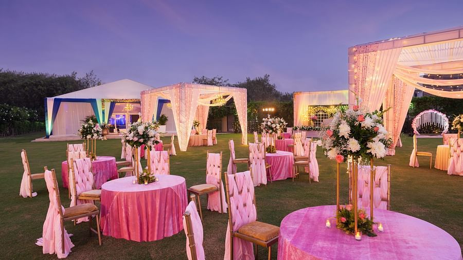 clusters of chairs and tables with pink covers and canopies lit up with decorative lights during the evening - The Hideaway Banquets & Lawns, Greater Noida