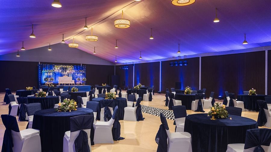 clusters of chairs and tables scattered across a room with chandeliers lighting up the hall - The Hideaway Banquets & Lawns, Greater Noida