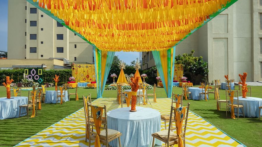 two tables with chairs in a cluster seated underneath a canopy during a sunny afternoon for shade - The Hideaway Banquets & Lawns, Greater Noida