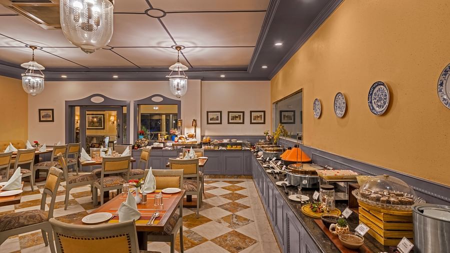 an image of a restaurant with a buffet setting and clusters of tables with chairs - The Manor, Kashipur