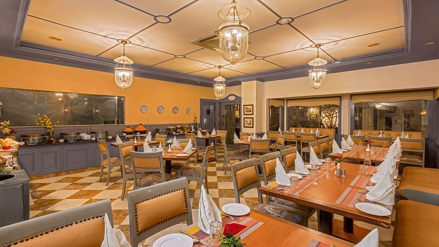 a view of a restaurant with a buffet setting and clusters of tables and chairs with lighting from four chandeliers - The Manor, Kashipur