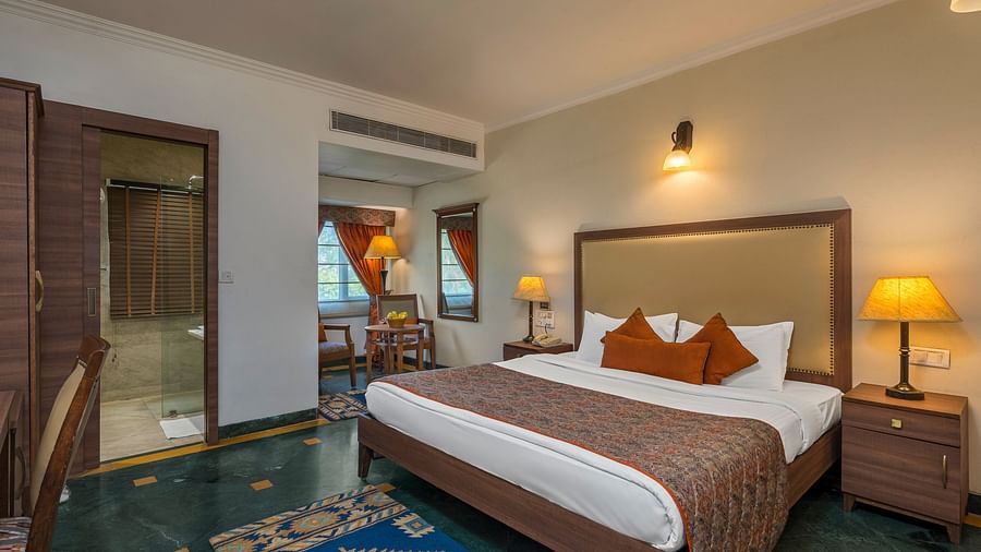 A bedroom with a large bed with side drawers placed on both sides of the bed, with an overhead lamp and side lamps - The Manor, Kashipur