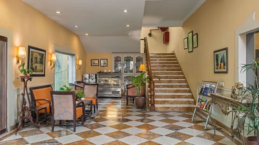 a lobby of a hotel with stairs leading up to the rooms on the right and chairs and tables for sitting on the left - The Manor, Kashipur
