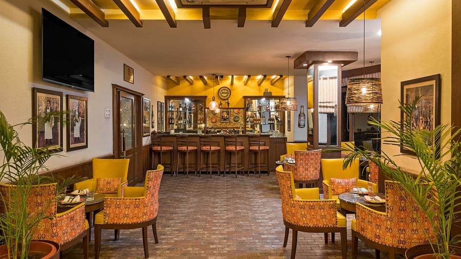 a view of clusters of chairs and tables with a bar counter at the end of the room - The Manor, Kashipur