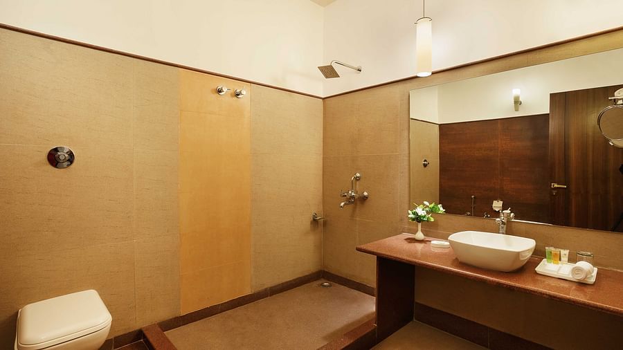 A bathroom featuring a shower space, a countertop with a washbasin, a lower vase on top, and various toiletries along with a face towel. A toilet is situated on the side