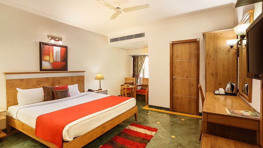 a view of a bedroom with a large bed facing a workdesk with a television above the workdesk - The Manor, Kashipur