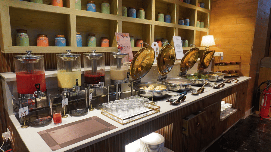 A well-stocked hotel breakfast buffet features various dispensers for juices and cereals, with shelves of mugs in the background  at the Meriton.