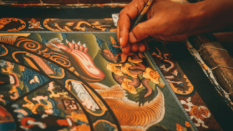 An artisan meticulously painting an intricate traditional Buddhist Thangka canvas with vibrant colors in a Kathmandu workshop, Nepal.