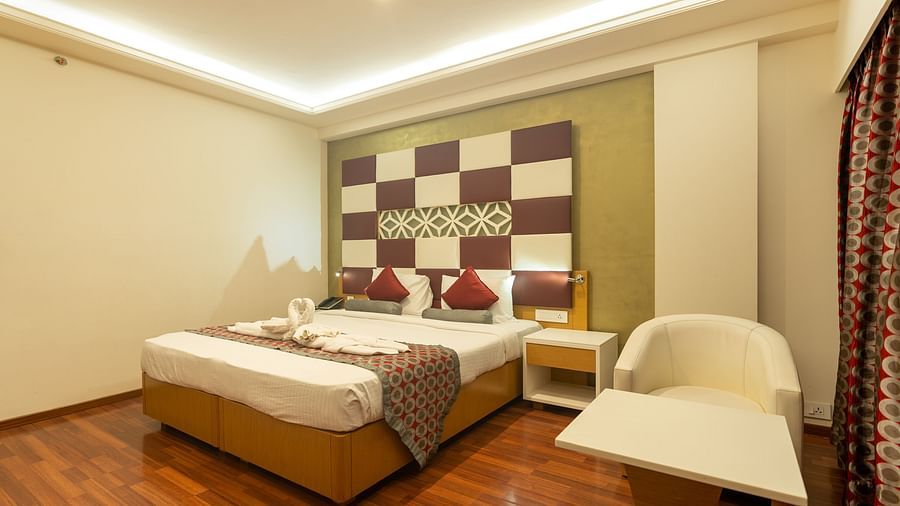 king size bed with side table and a chair and table at The President Hotel, Hubli