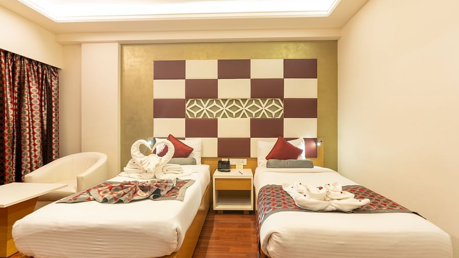 two single beds with a side table at The President Hotel, Hubli