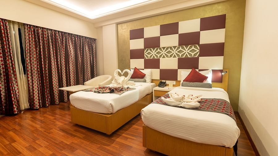 two single beds with a side table at The President Hotel, Hubli