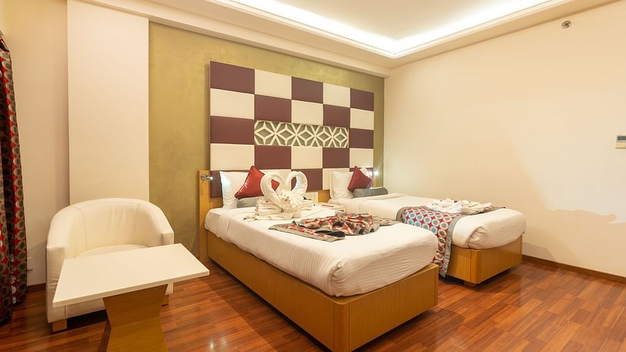 two single beds with a side table, a chair and a table at The President Hotel, Hubli