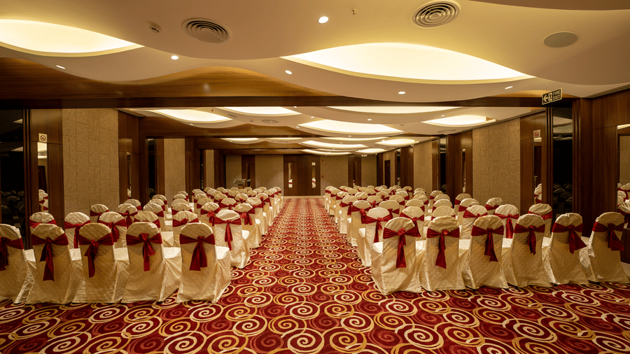 A banquet hall set for an event with chairs draped in white covers and a red-and-white patterned carpet - The President Hotel, Kumara Park, Bangalore