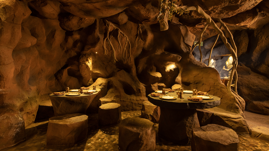 The cave-themed restaurant featuring rock-like tables and chairs, with animal print plates set on each table - The President Hotel, Kumara Park, Bangalore
