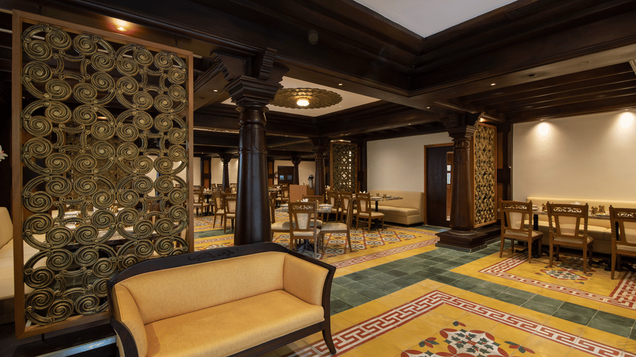 The seating area of a restaurant with printed flooring and a soft yellow illumination in the background -The President Hotel, Kumara Park, Bangalore