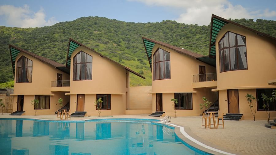 The Qualia Resort Club & Brewery, Udaipur presented with a long pool and lush green mountains in the backdrop.